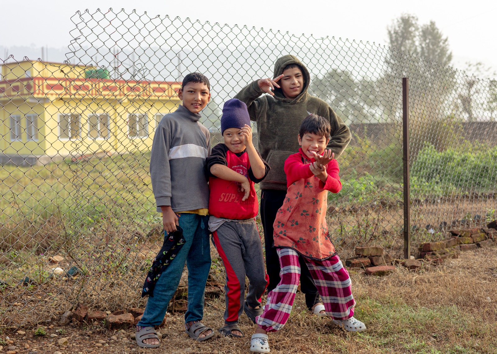 Four children standing outdoors beside a metal fence in Nepal